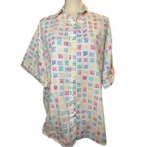 May include: A short-sleeved button-down shirt in white, featuring a repeating pattern of small, vertical, dashed lines in red, blue, yellow, and green. The shirt has a classic collar, a front button placket, and a relaxed, loose-fitting silhouette.