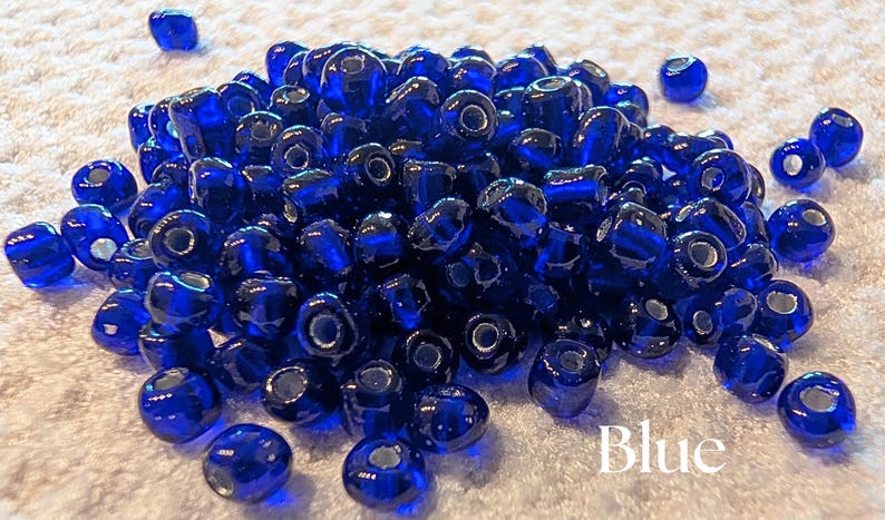 K&ouml;nnte beinhalten: Ein Haufen gl&auml;nzender, tiefblauer Glasperlen. Die Perlen sind rund mit einem Loch in der Mitte. Das Wort "Blue" ist in Wei&szlig; am unteren Rand des Bildes geschrieben. Diese Perlen eignen sich f&uuml;r die Schmuckherstellung und Bastelarbeiten.