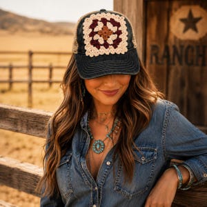 May include: A dark denim baseball cap featuring a square crochet patch on the front panel. The patch displays a geometric pattern in cream, maroon, and brown yarn. The cap has a structured brim and a mesh back panel, combining textile and mesh materials.