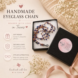 K&ouml;nnte beinhalten: Handgefertigte Brillenketten mit Perlen in einer Geschenkbox. Die Kette hat ein braunes Band mit blauen und silbernen Perlen. Die Box ist schwarz mit einem rosa-wei&szlig;en Aufkleber "Yarn Over Texas".