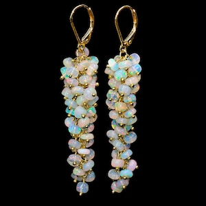 Peut inclure: Une paire de boucles d'oreilles pendantes composées de grappes de petites perles d'opale blanche iridescente suspendues à des crochets dormeuses dorés. Chaque boucle est formée de nombreuses pierres arrondies et translucides.