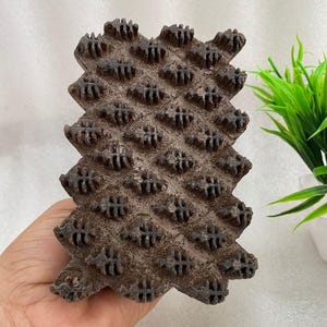 Könnte beinhalten: Ein dunkelbrauner Holzstempel mit einem sich wiederholenden geometrischen Muster aus kleinen, erhabenen, skelettartigen Blattformen in einem Raster. Der rechteckige Block hat eine texturierte, verwitterte Oberfläche für den Textildruck.