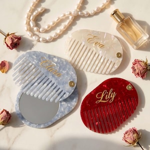 Puede incluir: Tres peines plegables ovalados con espejos, con patrones jaspeados en blanco, azul claro y rojo. Cada peine está personalizado con texto en cursiva dorada que dice Eva, Clara y Lily, e incluye un pequeño tornillo de pivote de metal dorado.