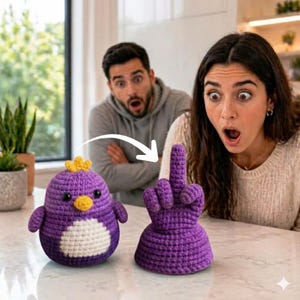 Puede incluir: Un pingüino de ganchillo morado con una corona amarilla y una barriga blanca está sentado junto a una mano de ganchillo morada que hace un gesto grosero. El pingüino tiene ojos negros y un pico amarillo. La mano tiene forma de dedo corazón.