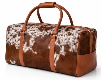 May include: A brown and white cowhide duffel bag with tan leather accents. The bag features two top handles and a shoulder strap. The bottom corners and straps are made of tan leather. The bag is designed for travel and has a zipper closure.