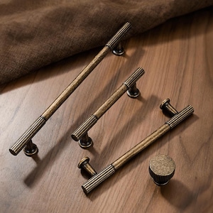 May include: A collection of antique bronze cabinet hardware, including three different-sized pulls and a round knob. The pulls have a ribbed design and are set against a wooden surface, showcasing a vintage aesthetic.