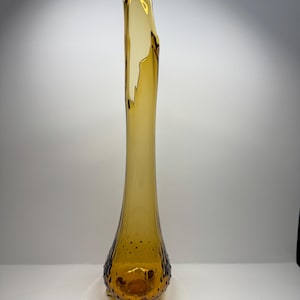 May include: A tall, amber-coloured glass vase with a slender body and a flared, irregular top. The vase features a textured, dotted pattern near the base and stands on three small feet. The glass has a glossy finish.