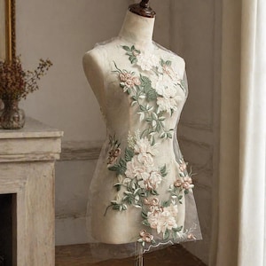 Puede incluir: Una aplicación de encaje floral con flores blancas y color rubor y hojas verdes. La aplicación se muestra en un maniquí, mostrando el delicado bordado y diseño. Ideal para proyectos de novia o artesanía.