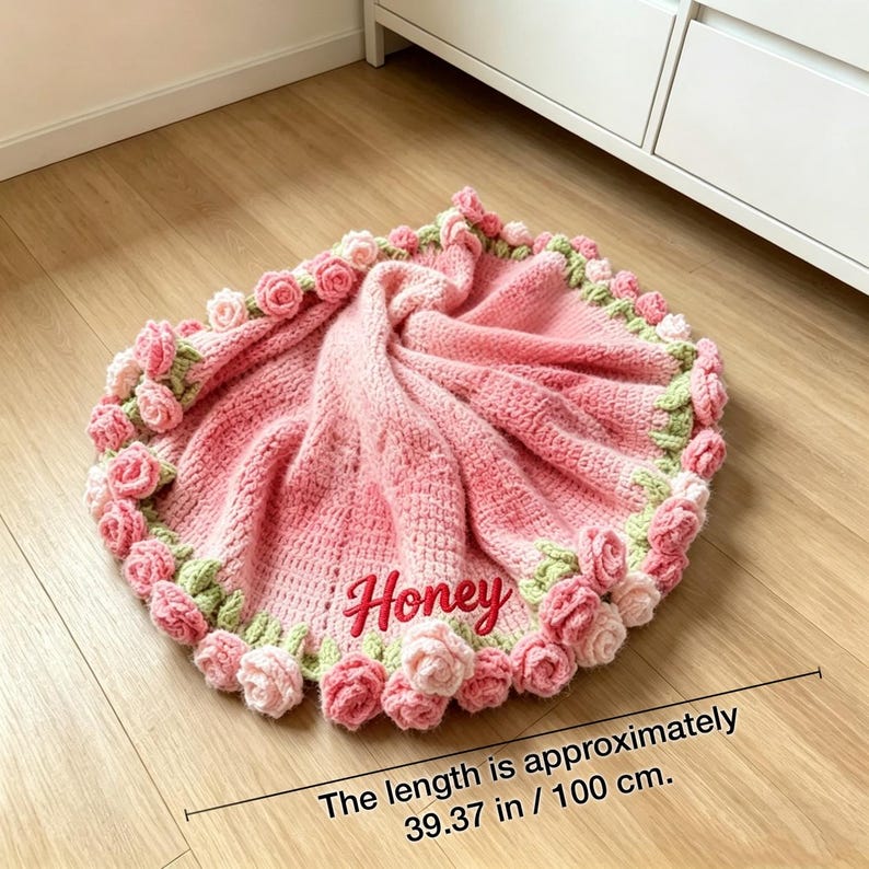 May include: A handmade pink crochet blanket with a rose border. The blanket is approximately 39.37 inches (100 cm) long and features the name "Honey" embroidered on it. The border is adorned with pink and green crochet roses.