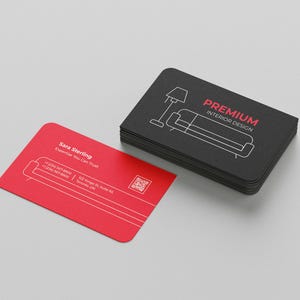 Könnte beinhalten: Ein Stapel schwarzer Visitenkarten mit abgerundeten Ecken, mit einer weißen Strichzeichnung einer Lampe und eines Sofas sowie den Worten "PREMIUM INTERIOR DESIGN" in Rot. Eine einzelne rote Visitenkarte mit weißem Text liegt neben dem Stapel.