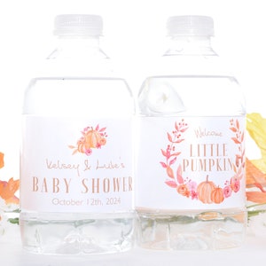 May include: Two clear plastic water bottles with labels. The labels are white with a watercolor design of fall leaves and pumpkins. The text on the labels reads "Kelsey & Luke's Baby Shower" and "Welcome Little Pumpkin".