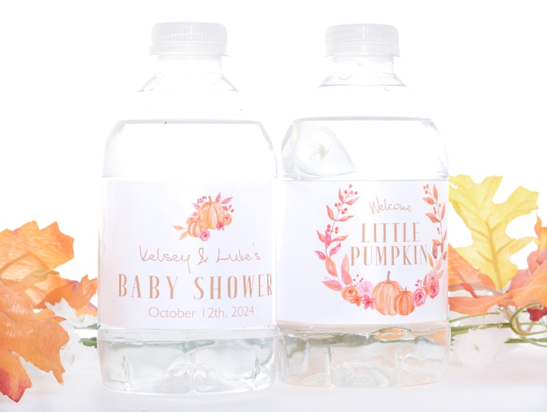May include: Two clear plastic water bottles with labels. The labels are white with a watercolor design of fall leaves and pumpkins. The text on the labels reads "Kelsey & Luke's Baby Shower" and "Welcome Little Pumpkin".