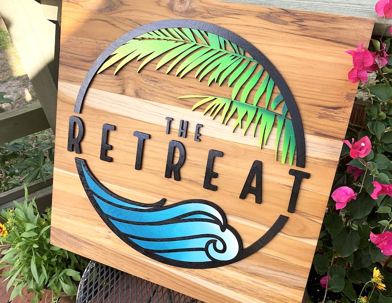May include: A wooden sign with a black circle containing a green palm tree and a blue wave. The text "THE RETREAT" is in black letters.