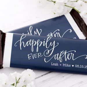 May include: Two chocolate bars wrapped in blue paper with white text that reads "happily ever after" and the names "Leah + Mike" and the date "06.20.18".