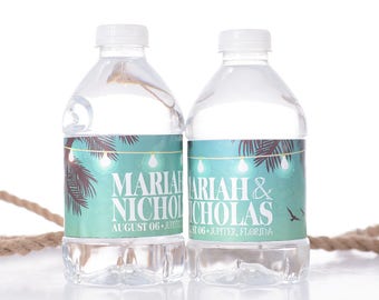 May include: Two clear plastic water bottles with personalized labels. The labels feature a tropical palm tree design with string lights and the text "Mariah & Nicholas" with the wedding date "August 06, Jupiter, Florida".