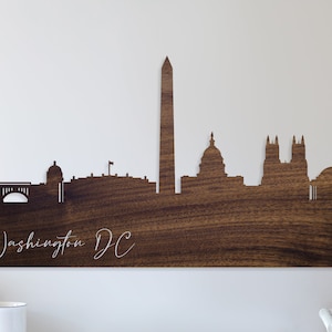 May include: A wooden wall art piece featuring a silhouette of the Washington, D.C. skyline. The skyline includes the Washington Monument, the Capitol Building, and the National Mall. The text "Washington DC" is written below the skyline.