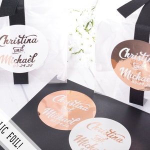 May include: Three round wedding favor stickers with the text "Christina and Michael 03.24.22" in a cursive font. Two stickers are rose gold foil and one is white.
