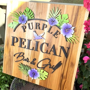 May include: Wooden sign with the text "Purple Pelican Bar & Grill" in black lettering. The sign is decorated with tropical leaves and purple hibiscus flowers.