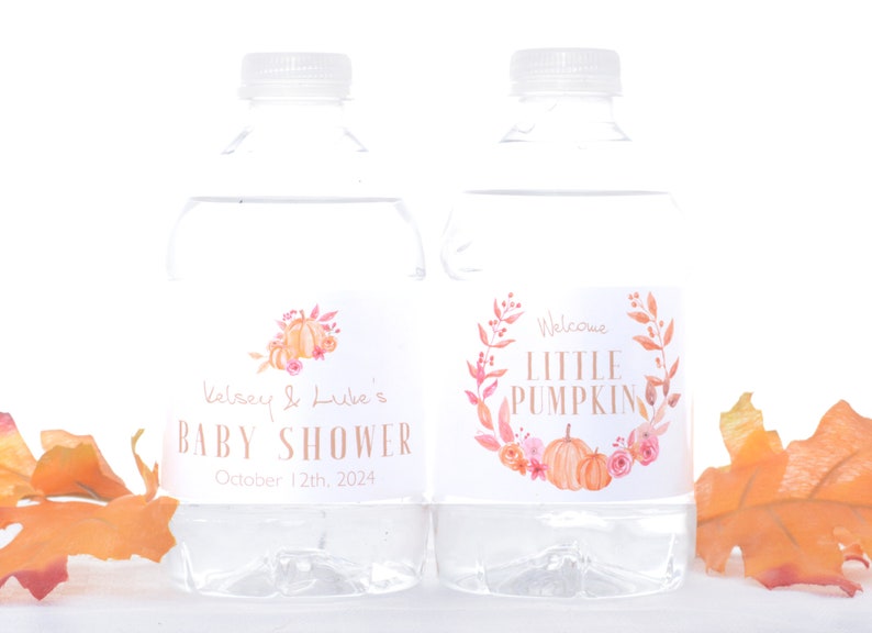 May include: Two clear plastic water bottles with labels. The label on the left bottle says "Kelsey & Luke's Baby Shower October 12th, 2024". The label on the right bottle says "Welcome Little Pumpkin" with a watercolor illustration of pumpkins and flowers.
