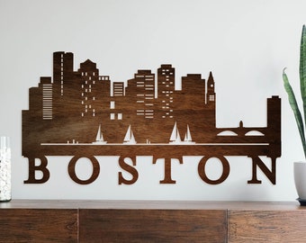 May include: A wooden wall decor featuring a silhouette of the Boston skyline with the word "BOSTON" written below. The skyline includes several buildings, a bridge, and sailboats.