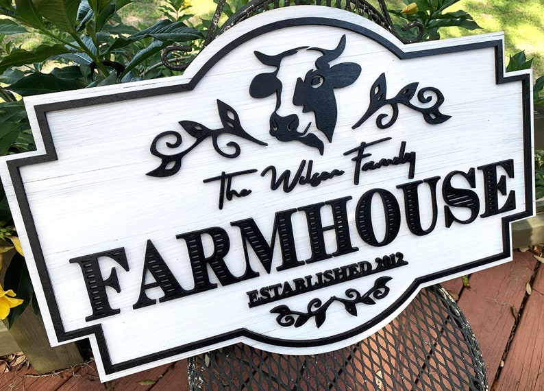 May include: White farmhouse sign with black lettering and a black silhouette of a cow. The sign reads "The Wilson Family Farmhouse Established 2012".