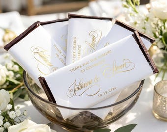 Op de afbeelding: Meerdere rechthoekige chocoladerepen verpakt in wit papier met goudkleurige foliebedrukking. De tekst luidt "Thank you for coming to celebrate" gevolgd door de namen "Julianne & Steven" en de datum "18-10-2024" in een sierlijk lettertype.