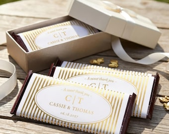 Op de afbeelding: Rechthoekige chocoladerepen verpakt in wit papier met gouden verticale strepen en een centraal ovaal etiket. Het etiket bevat de tekst A sweet thank you, de initialen C | T, de namen CASSIE & THOMAS en de datum 18.06.2027 in goud.