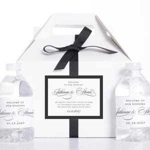 May include: White wedding favor box with a black ribbon and a tag that reads "Welcome to our wedding" with the names Julianne & Steven and the date 05.18.2027. Two water bottles with matching labels are on either side.
