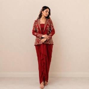 May include: A deep red ensemble consisting of a long-sleeved blazer and a matching draped skirt. The blazer features intricate gold-toned embroidery along the lapels and sleeves. The skirt has a layered, cascading ruffle design in the front.