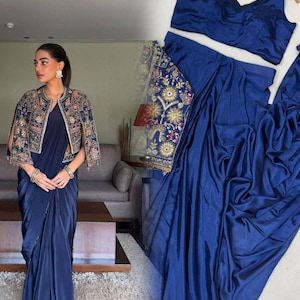 May include: A navy blue saree set, including a draped skirt, a matching sleeveless top, and an embroidered jacket. The jacket is adorned with gold, blue, and other coloured embroidery. The saree is made of a smooth, flowing fabric.