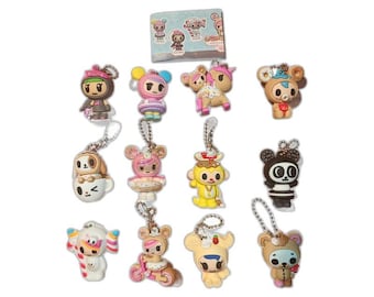 May include: A collection of eleven small, colorful character keychains featuring various designs including animals, food-themed figures, and whimsical creatures. Each keychain includes a metal ball chain attachment and a small rectangular paper card.