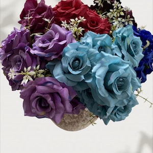 Puede incluir: Un ramo de rosas artificiales en varios colores. El arreglo incluye rosas moradas oscuras, rojas y azul claro, complementadas con pequeñas flores blancas. Las flores están dispuestas en un jarrón moteado de color claro.