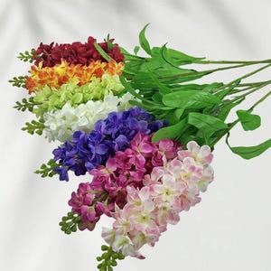 May include: A selection of artificial flower stems in a rainbow of colours. The flowers are arranged in a gradient, including red, orange, yellow, green, white, purple, pink, and light pink. Green leaves and stems are also visible.
