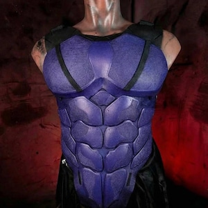 以下が含まれることがあります： 紫と黒の胸部アーマーで、コスプレやコスチューム用と思われる。アーマーは筋肉質な胴体を模倣するように設計されており、セグメント化されたプレートとテクスチャ加工された表面を備えています。肩の部分は黒で、全体的なデザインは未来的です。