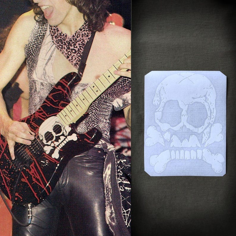May include: Black electric guitar with red splatter design and a skull and crossbones graphic. The guitar is being played. A skull and crossbones design is also on a white rectangle.