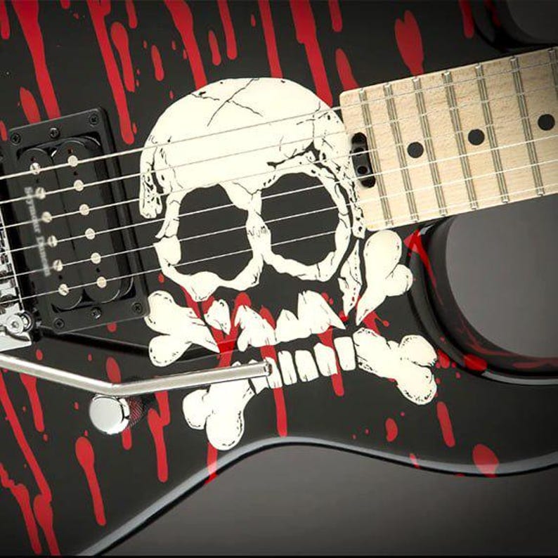 May include: Black electric guitar with a skull and crossbones design. The guitar features a white skull graphic with red blood splatter accents. The fretboard is light-colored wood, and the strings are visible.