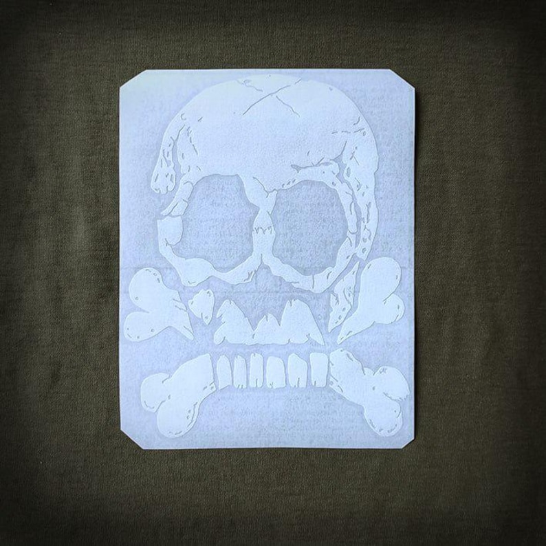 May include: White skull and crossbones design on a rectangular sticker. The skull has visible cracks and detailed features, with crossbones beneath. The sticker is on a dark green background, suitable for apparel or accessories.