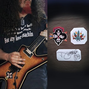 May include: The image shows a musician playing a brown and yellow electric guitar. The musician wears a black t-shirt with the text "a bell gas tank For my love machin". There are three patches: a Kiss band patch, a cannabis leaf patch, and a signed patch.