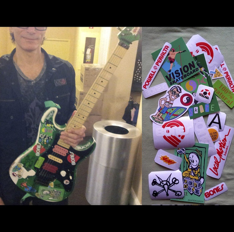 May include: An electric guitar with a green and black design, covered in stickers, held by a person. Stickers include "BONES", "POWELL PERALTA", and "VISION SKATEBOARD". A pile of stickers is also visible.