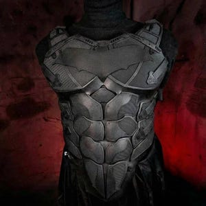 Puede incluir: Una armadura de pecho negra y texturizada con un diseño segmentado. La armadura presenta un prominente símbolo de murciélago en el pecho y los hombros. La estética general sugiere un tema de superhéroe o cosplay.