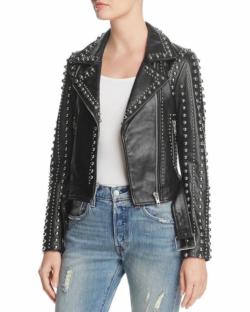 May include: Black leather jacket with silver stud embellishments. The jacket features a classic biker style with a notched collar, asymmetrical zip closure, and a belt at the waist. The sleeves and shoulders are heavily studded.
