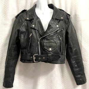 May include: Black leather motorcycle jacket with a notched collar, asymmetrical zipper, and a belted waist. The jacket features silver hardware, including zippers and snaps, and has a classic biker style.