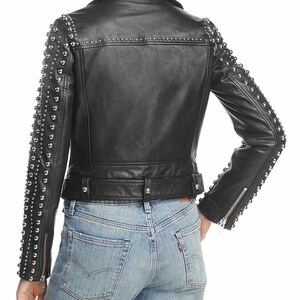 May include: Black leather jacket with silver stud embellishments on the shoulders and sleeves. The jacket has a notched collar, a belted waist, and zippered sleeves. The model is wearing blue jeans.