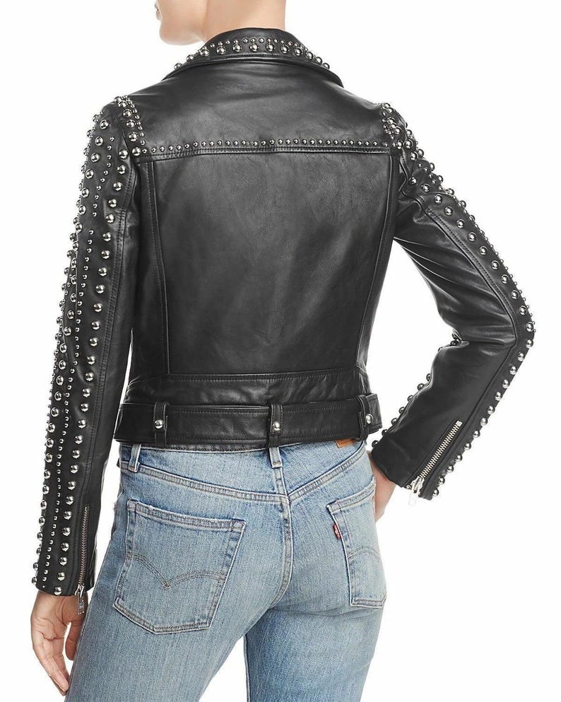 May include: Black leather jacket with silver stud embellishments on the shoulders and sleeves. The jacket has a notched collar, a belted waist, and zippered sleeves. The model is wearing blue jeans.