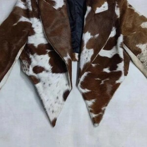 May include: A brown and white cowhide jacket with a notched collar and a black lining. The jacket has a unique pattern and a tailored fit, perfect for adding a touch of rustic flair to any outfit.