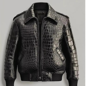 Könnte beinhalten: Schwarze Lederjacke mit Krokodilleder-Textur. Die Jacke hat einen Kragen, einen Reißverschluss vorne und gerippte Bündchen und Saum. Sie hat zwei Vordertaschen und Schulterklappen.