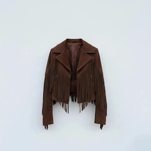 Puede incluir: Chaqueta de ante marrón con largos flecos en las mangas y el pecho. La chaqueta tiene un cuello clásico y un corte entallado, perfecto para un look bohemio elegante. La chaqueta se muestra sobre un fondo blanco.