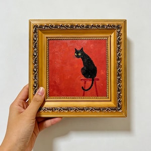 May include: An oil painting in a decorative gold frame featuring a black cat with yellow eyes sitting on a red stool against a textured red background. The painting includes the text SALARCOLLECTIONS at the bottom of the image.