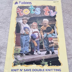 May include: A Patons knitting pattern booklet titled Tots TV PBN P 339. The cover features three children wearing sweaters with character designs, holding handmade dolls. The text reads Knit N' Save Double Knitting on a yellow background.