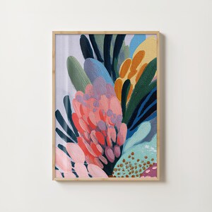 Op de afbeelding: Abstracte bloemenkunstprint in een houten lijst. Het kunstwerk toont een levendige compositie van kleurrijke penseelstreken in tinten roze, oranje, blauw, groen en geel. Het schilderij heeft een textuur, met zichtbare penseelstreken die diepte en dimensie creëren.